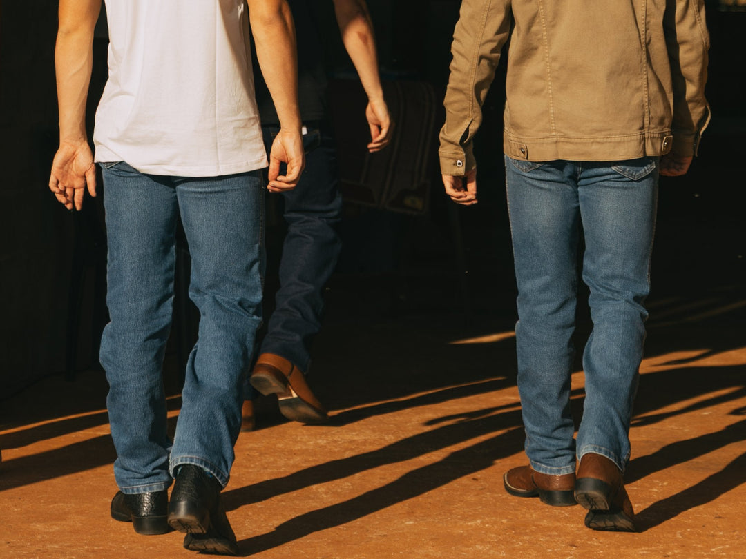 Homens de calça jeans caminhando com bota e botina de couro, com a barra da calça por cima do cano