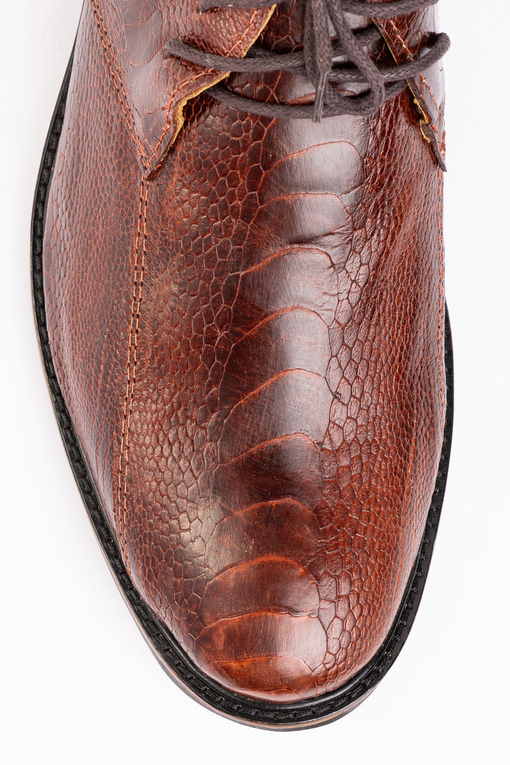 Detalhe macro das escamas naturais do couro de canela de avestruz caramelo no bico redondo da ankle boot Strut