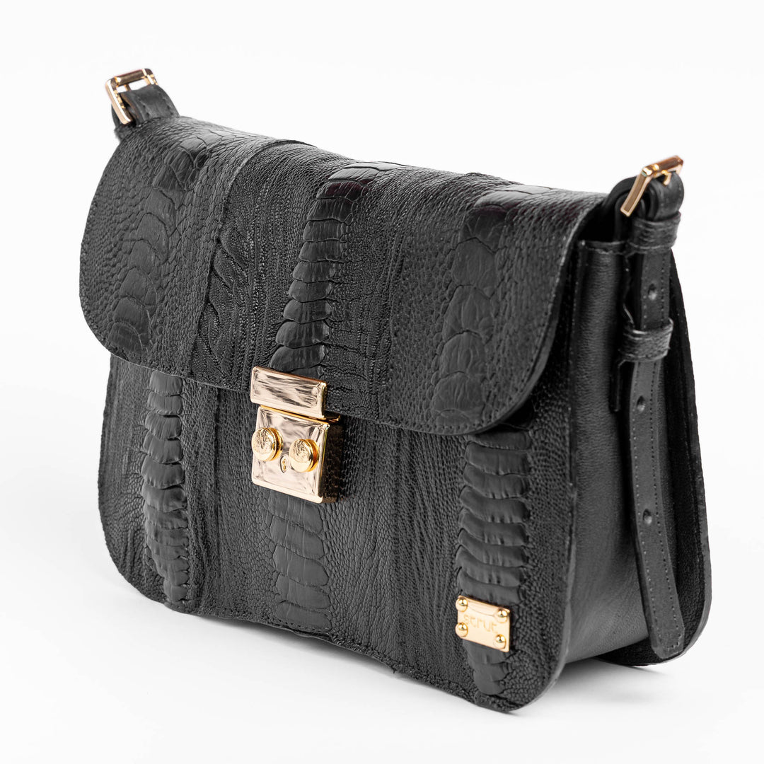 Bolsa baguete Strut em canela de avestruz preto vista três quartos com alça ajustável