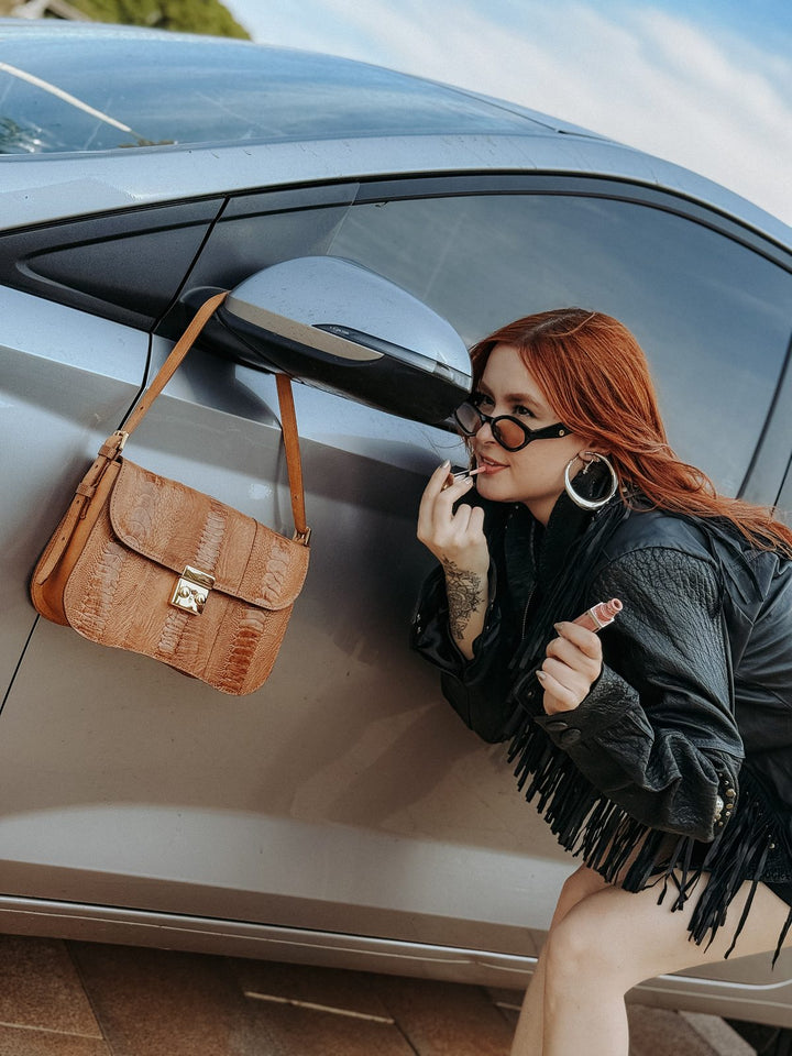 Bolsa baguete Strut em couro de canela de avestruz caramelo apoiada no espelho do carro