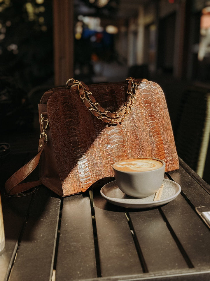 Bolsa social transversal Strut em canela de avestruz com alça de corrente dourada sobre mesa de café