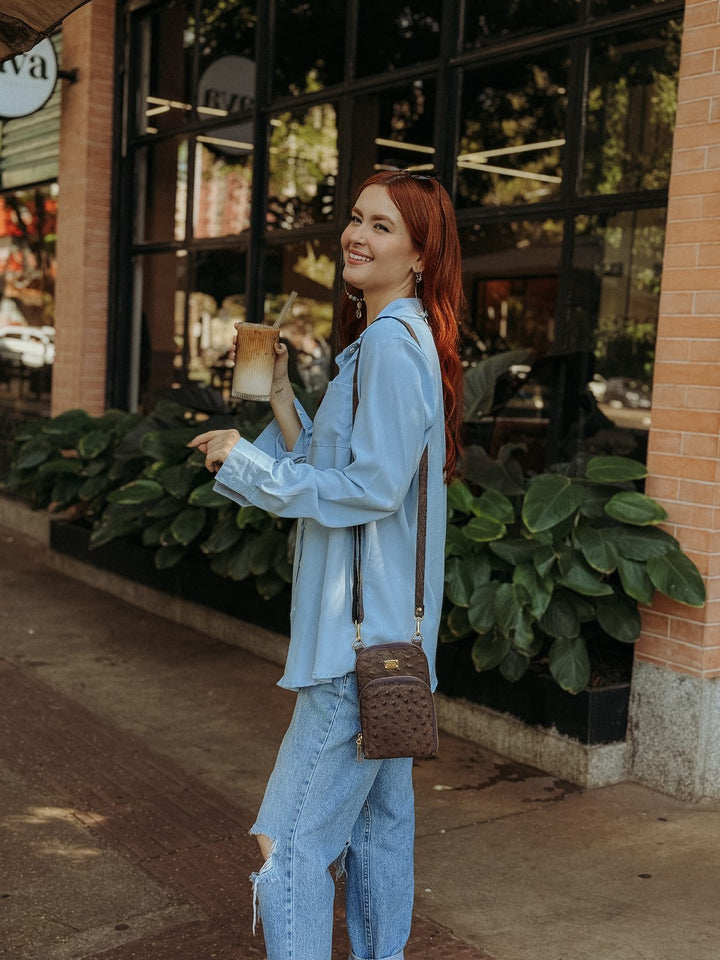 Mini bolsa carteira Strut em couro de avestruz cheio caramelo usada a tiracolo com jeans e camisa azul