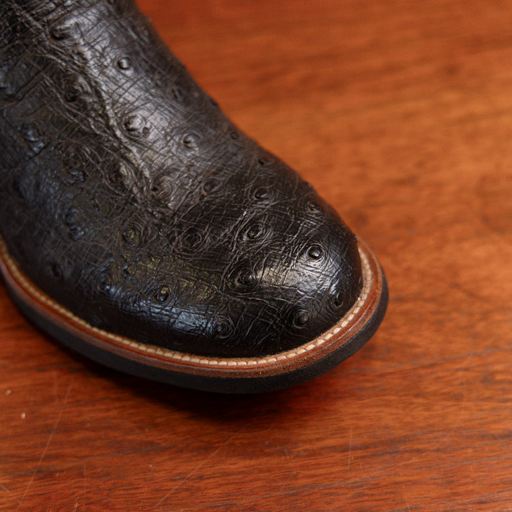 Detalhe do bico redondo da bota masculina strut em couro de avestruz cheio preto com cano vermelho bordado azul e amarelo