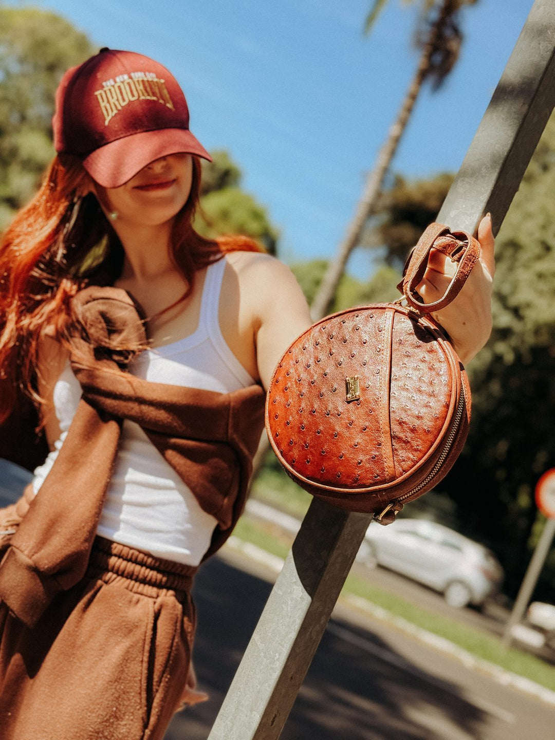 Bolsa redonda Strut em couro de avestruz cheio caramelo em uso, mostrando o tamanho real