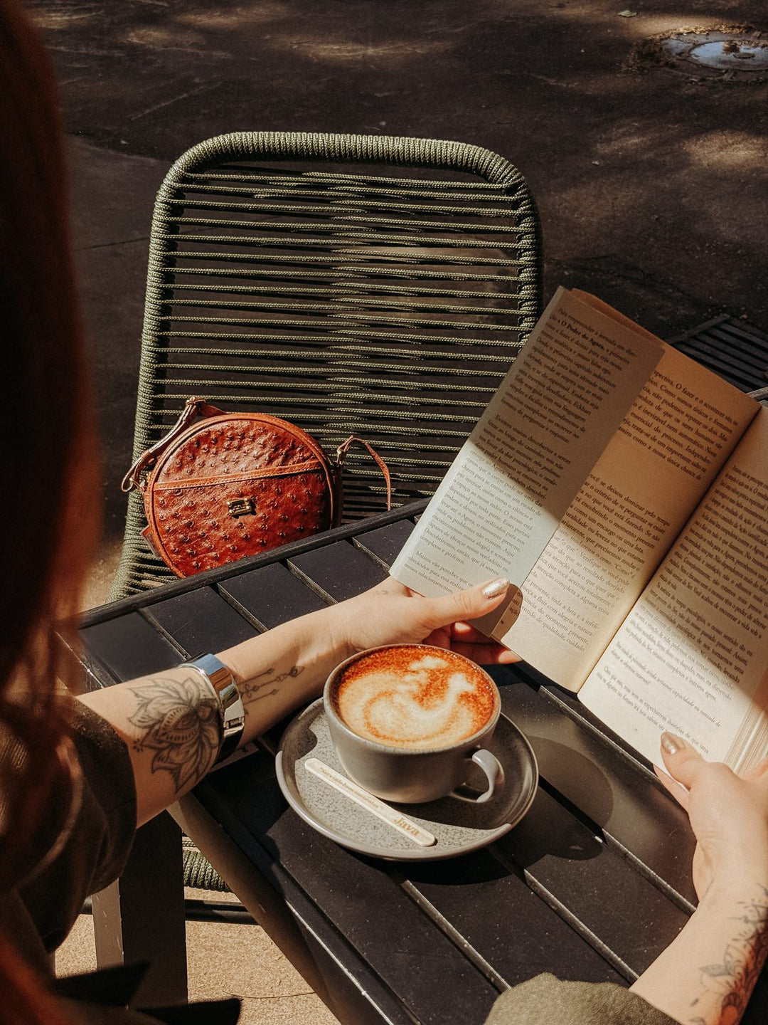 Bolsa redonda Strut em couro de avestruz cheio caramelo sobre mesa de café com livro