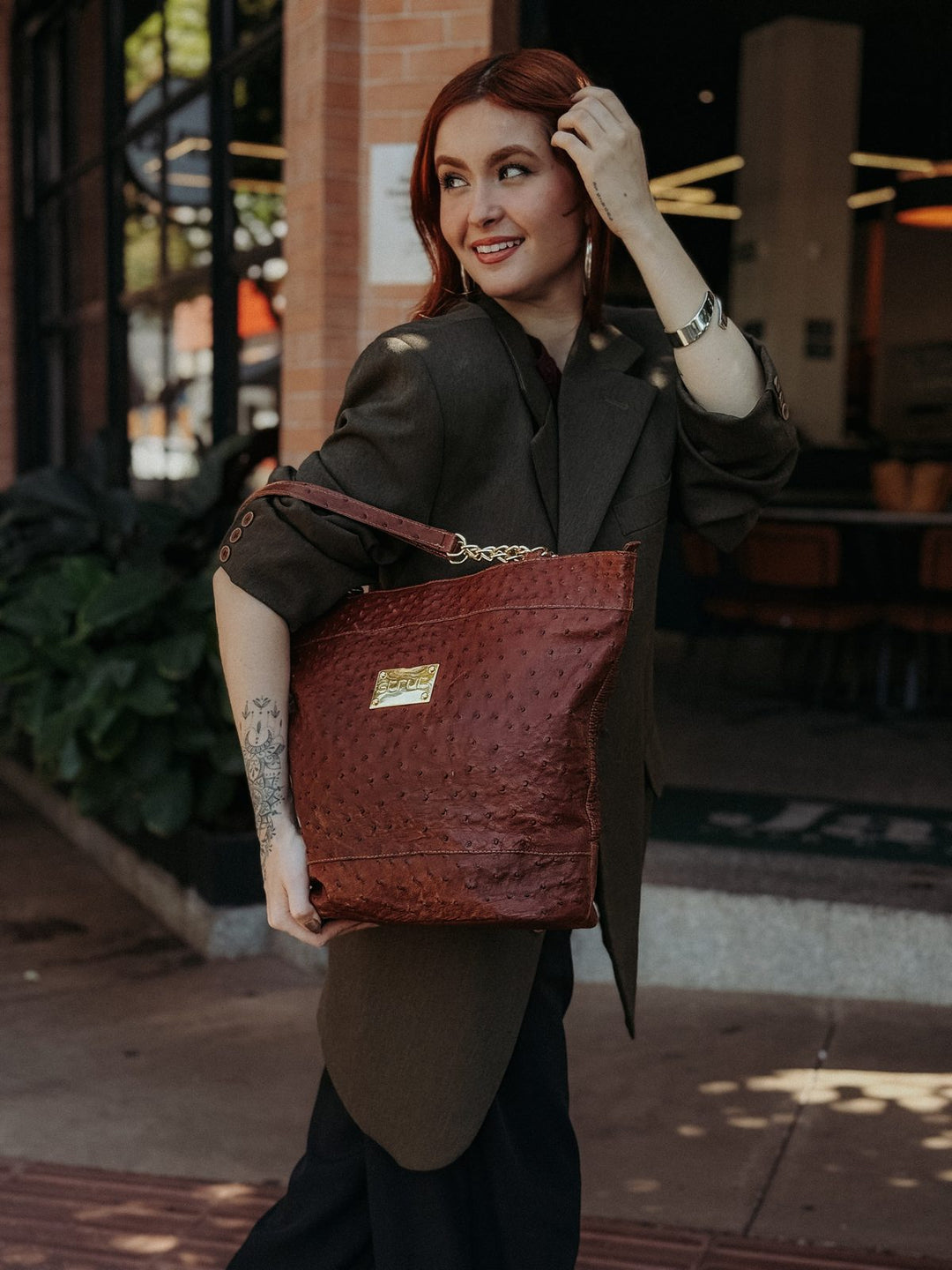 Bolsa social feminina Strut em couro de canela de avestruz caramelo usada no ombro com blazer